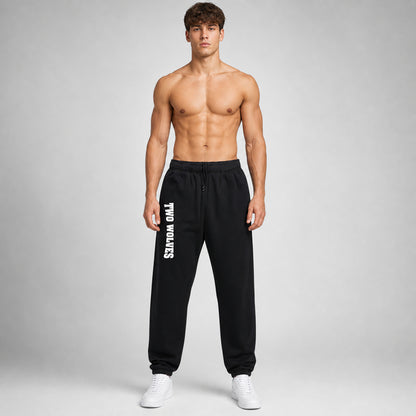 Black Two Wolves track pants with white logo on leg, worn by male model